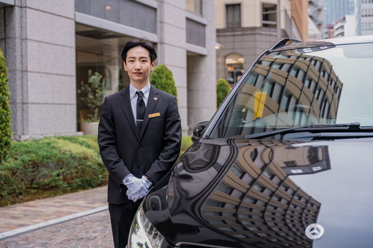 RydAgent chauffeur in a suit and white gloves beside a black Mercedes